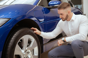 Handsome bearded man examining tires on a new car on sale at the dealership