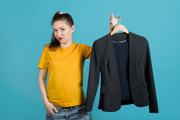 A girl in bright clothes holds a hanger with a business suit and shows her dislike