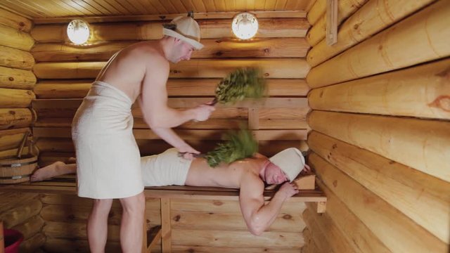 Athletic men soaring in a sauna with brooms.