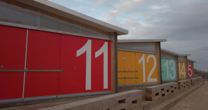 Bright coloured modern numbered Beach huts dolly shot filmed on cold winter afternoon