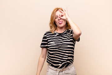 middle age woman smiling happily with funny face, joking and looking through peephole, spying on...