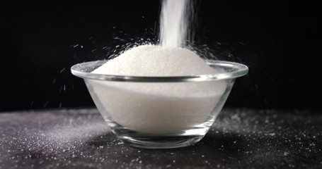 White sugar or salt falling in the bowl, black background