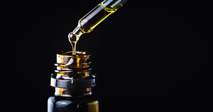 CBD Hemp oil, Hand holding droplet of Cannabis oil against black background. Alternative Medicine