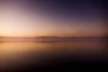 Fototapeta premium Early morning on the lake with a pink dawn and shrouded haze of mist, a mesmerizing mysticism of nature