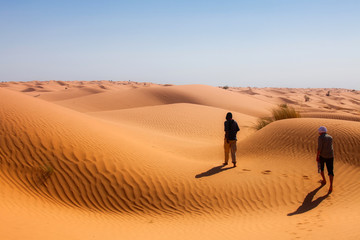 two people walking through the sunny desert and casting dark shadows on the orange sand