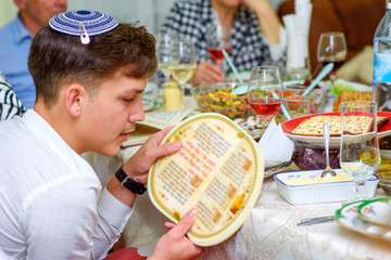 Jewish family celebrate Passover Seder reading the Haggadah. Young jewish boy with kippah reads the...