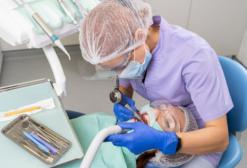 The dentist using specialized tools treats caries in the patient’s oral cavity using new technologies in dentistry.