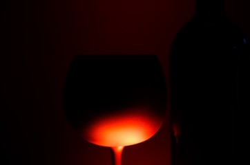 Close up of silhouette isolated wine glass and bottle illuminated by red shiny light, black background