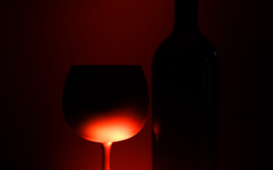 Close up of silhouette isolated wine glass and bottle illuminated by red shiny light, black background