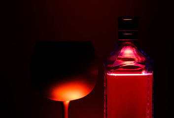 Close up of silhouette isolated wine glass and bottle illuminated by red shiny light, black background