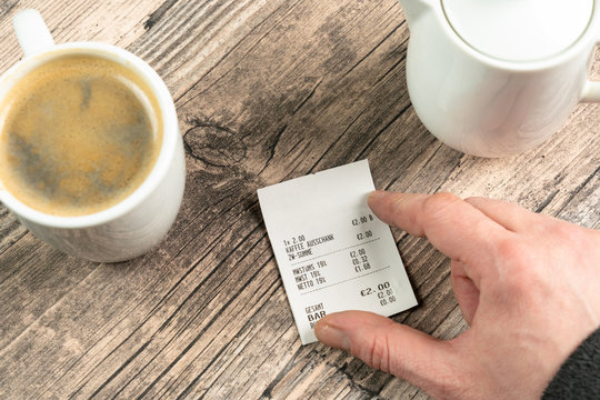 a hand on a receipt on a table with a cup of coffee