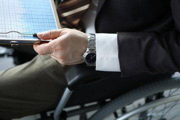 Disabled man holds business chart in hand while sitting wheelchair closeup office background....