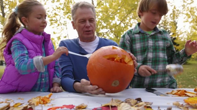 Grandfather and grandchildren carving pumpkin. CU, RL pan, real time.