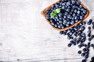 Freshly picked blueberries in wooden bowl on white table. Juicy and fresh blueberry with green leaves at rustic board. Bilberry antioxidant healthy forest food. Top view photo.