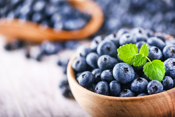 Blueberries in wooden bowl with mint leaf on top. Blueberry forest fruit close up or detail on white board.