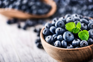 Freshly picked blueberries in wooden bowl on white table. Juicy and fresh blueberry with green leaves at rustic board. Bilberry antioxidant healthy forest food.