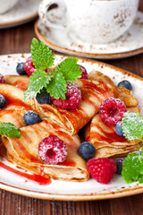 Pile of small homemade pancakes with berries and  syrup on wooden table