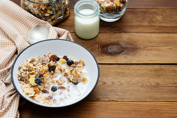 Whole oats breakfast, granola with dried fruit and blueberry, milk and honey. Wooden background. Copy space.