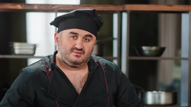 Portrait of positive male chef in uniform posing at kitchen. Medium close up shot on 4k RED camera
