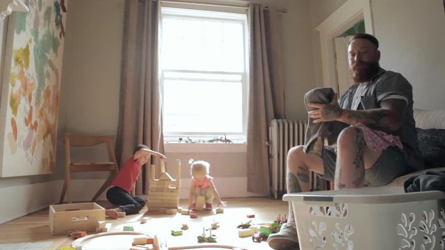 Father Folding Laundry Near Children Playing With Wood Blocks