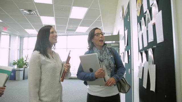 College Students Checking Bulletin Board In Corridor