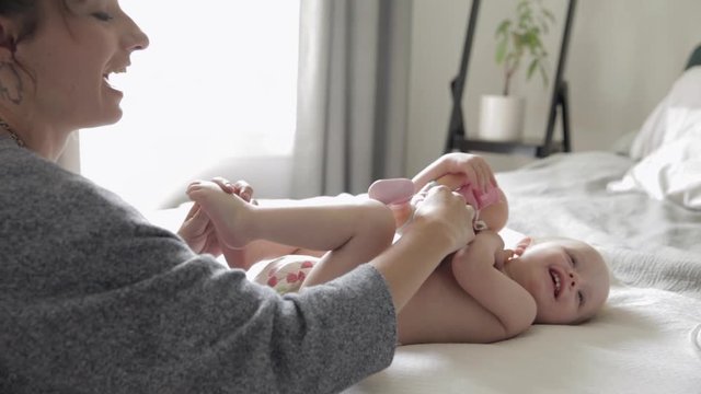Mother playing with baby daughter holding doll on bed