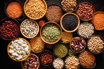 Legumes, a set consisting of different types of beans, lentils and peas on a black background, top view. The concept of healthy and nutritious food - obrazy, fototapety, plakaty