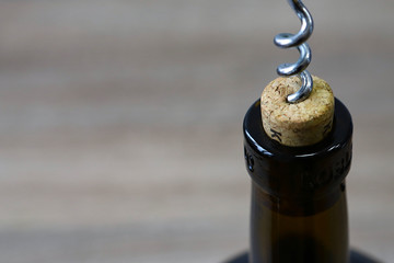 Metal corkscrew with a wooden handle screwed into a bottle stopper with red dry wine. Healthy use...
