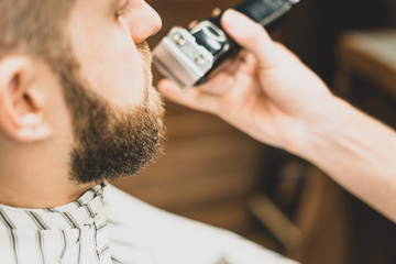 Beauty shop for men. Shaving a beard in a barbershop. Barber cuts his beard with a razor and clipper. close up Brutal haircuts. Hairdresser equipment. Selective focus.