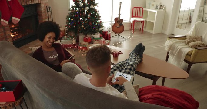 Young couple relaxing, using smart phone and digital tablet in Christmas living room
