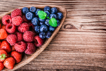 Forest fruits in wooden bowl. Blueberries, raspberries, strawberries on vintage table.