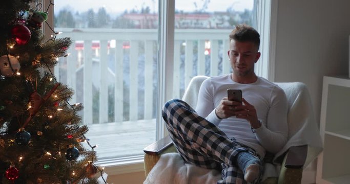 Young man texting with smart phone near Christmas tree