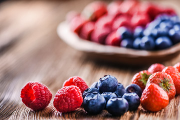 Forest fruits in wooden bowl. Blueberries, raspberries, strawberries on vintage table.