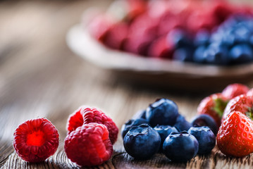Forest fruits in wooden bowl. Blueberries, raspberries, strawberries on vintage table.