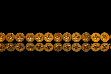 Bronze screws under a screwdriver on a black background with reflection.