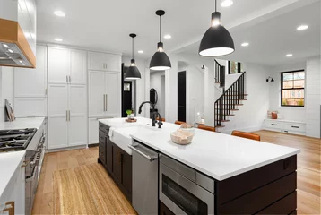 Fotobehang Beautiful white kitchen with dark accents in new modern farmhouse style luxury home. Features large island with farmhouse sink, dishwasher, microwave and view of living room and stairs. © bmak