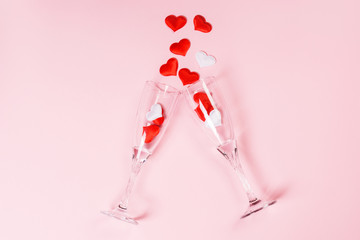Two glass of champagne with a splash of red and white heart shaped confetti