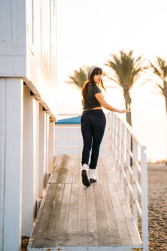 Young Brunette woman with long hair and hat stands on the beach of Los Angeles in to a the lifeguard booth