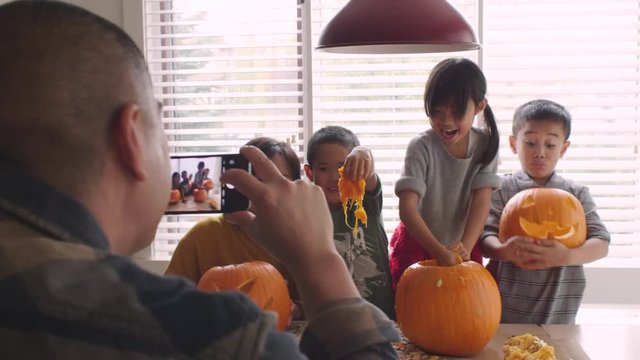 Father photographing family carving Halloween pumpkins