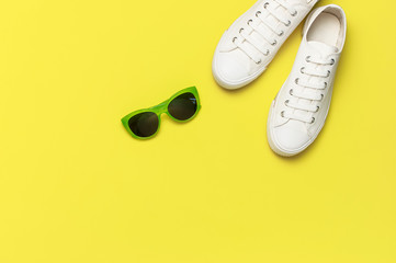 White female fashion sneakers, trendy sunglasses, white T-shirt on yellow background. Flat lay top view copy space. Women's shoes, accessories. Stylish white sneakers. Creative concept Fashion blog