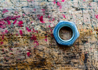 Hex nut isolated on stained, used, cut, wooden workbench surface background. Selective focus on nut shiny surface.