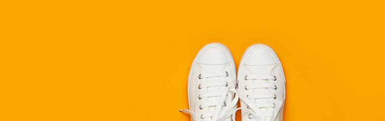 White female fashion sneakers on yellow orange background. Flat lay top view copy space. Women's shoes. Stylish white sneakers. Fashion blog or magazine concept. Minimalistic shoe background, sport