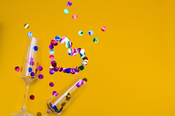 two glass champagne glasses not with a yellow background strewn with confetti, shiny circles, Valentine's day concept, wedding day, lovers' date, place of copy, heart from confetti