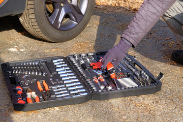 Сar driver using different repair tools for repairing a car. Tool set near the orange auto. Closeup picture of mechanic tools in box.