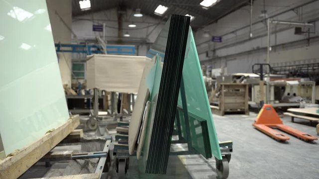 Warehouse of glass panels. Glass sheets stacked one on another on a glass holding cart in the industry workshop. Orange manual forklift in the background. 
