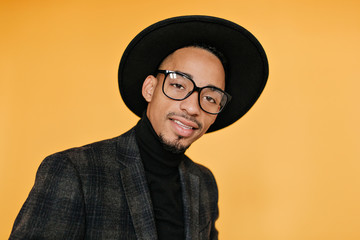 Close-up portrait of black male model in black hat. Indoor photo of cheerful young man with brown skin.