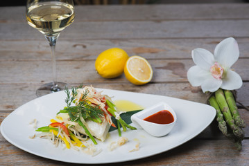 White fish seabass fillet with vegetables and white wine on a wooden table in a restaurant with decor. Tasty and healthy food. A cozy evening in a restaurant during a date. Beautiful table setting.