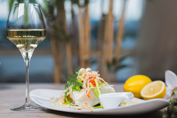 White fish seabass fillet with vegetables and white wine on a wooden table in a restaurant with decor. Tasty and healthy food. A cozy evening in a restaurant during a date. Beautiful table setting.