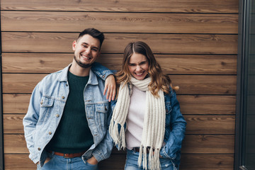 Blissful young people in denim jackets standing on wooden background. Indoor portrait of caucasian blithesome woman having fun in weekend with boyfriend.