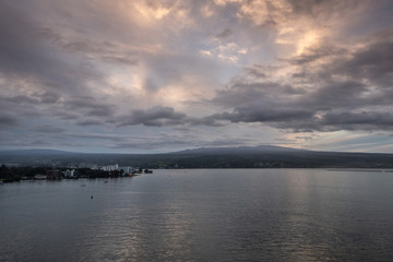 Fototapeta na wymiar Hilo, Hawaii, USA. - January 14, 2020: Spectacular lighter evening cloudscape with yellow sunlight patches over town and volcano on horizon.